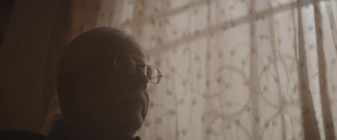 A man wearing glasses sits near a window