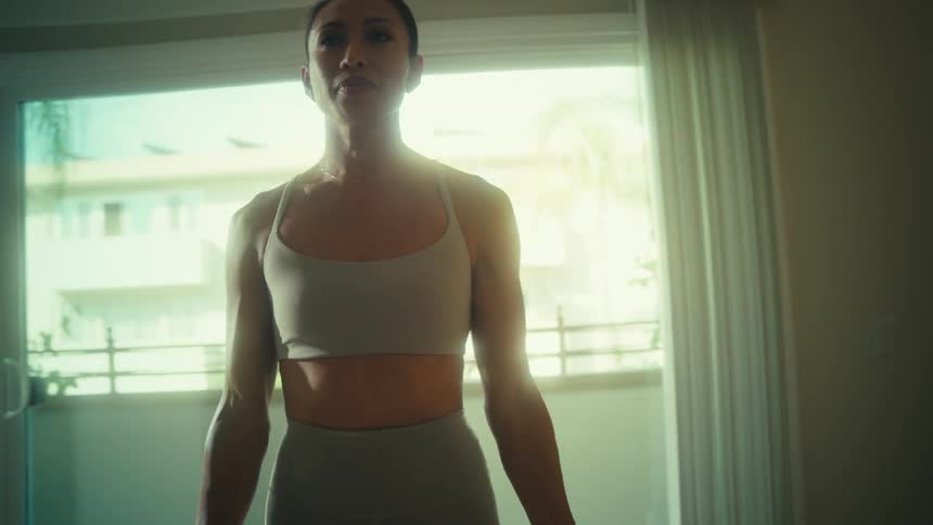 A young woman lifts weights with both hands while exercising indoors during daytime