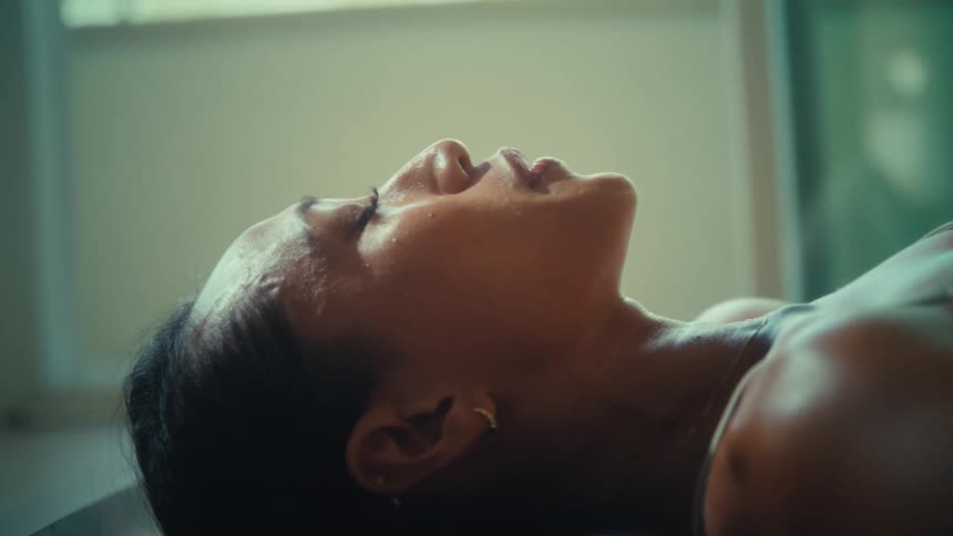 A woman is seen lying down with her eyes closed looking up possibly in a state of rest or reflection the closeup shot focuses on her face and shoulder with soft lighting illuminating her features