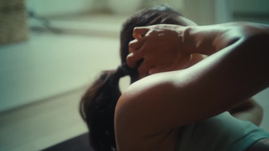Woman doing abdominal crunches indoors with focused expression and defined arm muscles highlighted by soft lighting