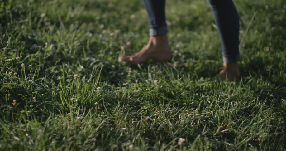 A young lady walking barefoot on a grassland at midday
