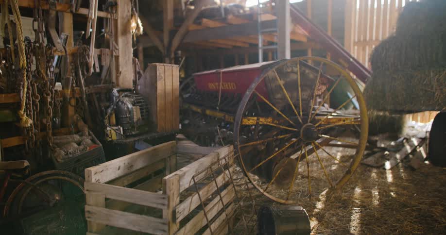 Hay covers the floor in a barn with various pieces of farming equipment stored inside