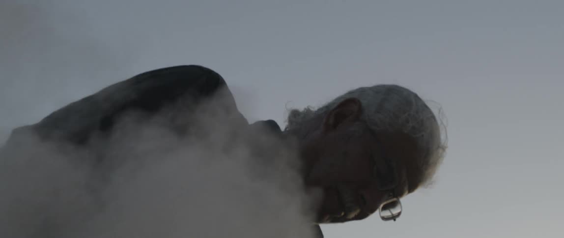 A man uses a power tool to grind a rock while dust flies all around