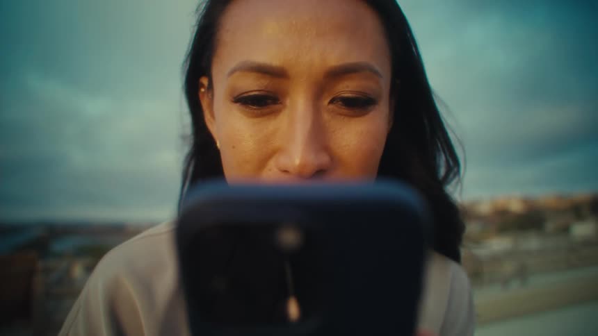 An asian women is holding a smartphone against a blurred urban backdrop under an overcast sky