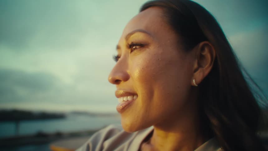 Woman smiling as she gazes into the distance with the ocean and city behind her