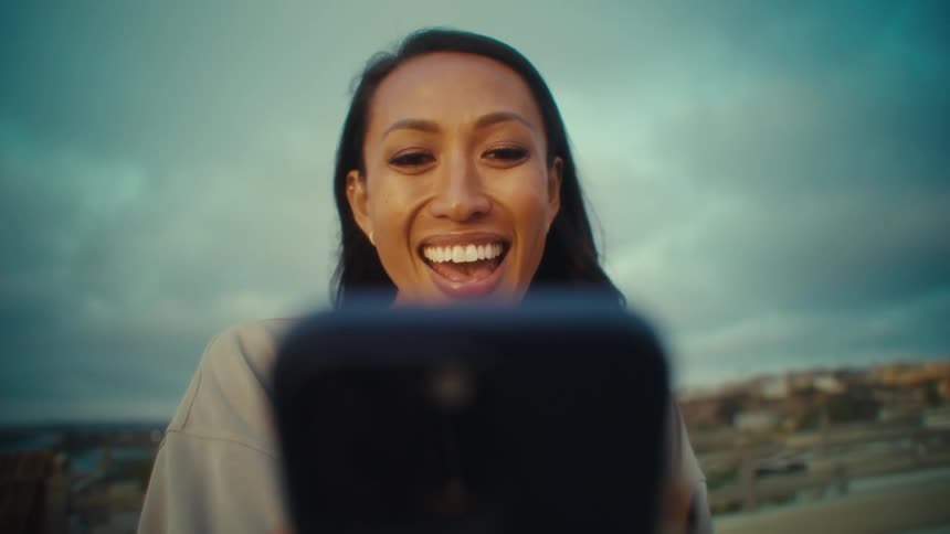 Close up of a young woman smiling and waving on a video call with her mobile phone while sitting outdoors during daytime