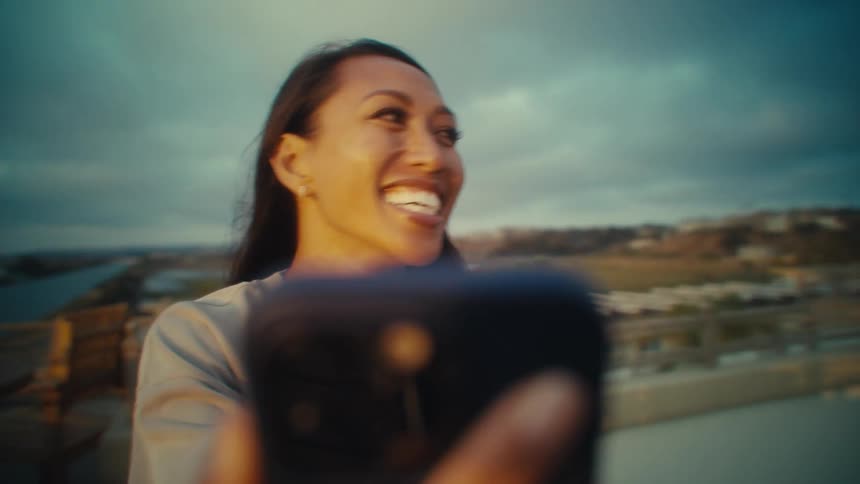 A woman laughs joyfully while holding her phone up outdoors