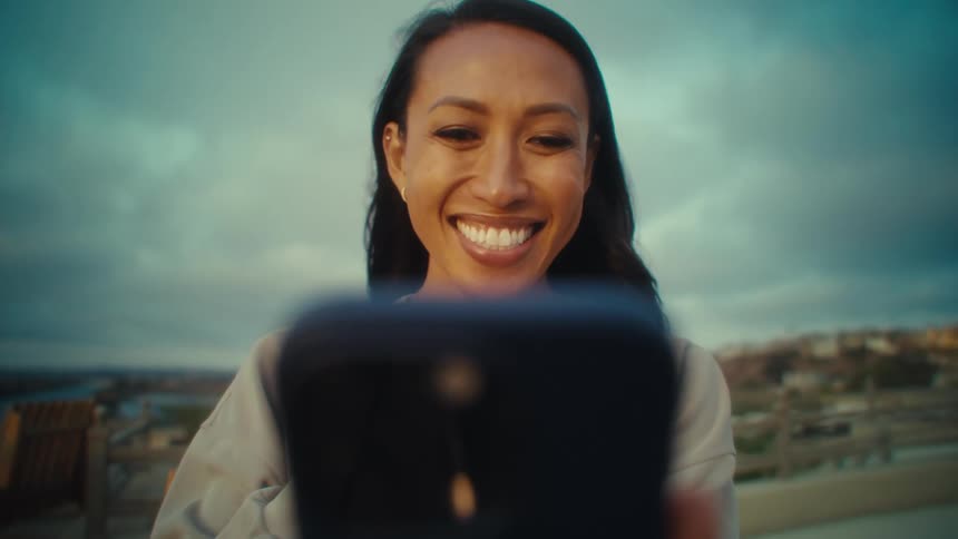 A smiling woman is on a video call outdoors