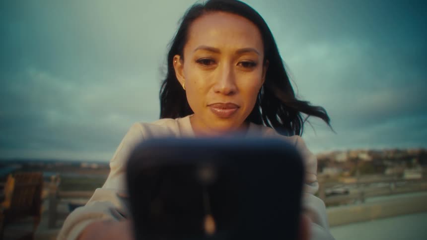A focused woman looks at her phone outdoors bathed in goldenhour light
