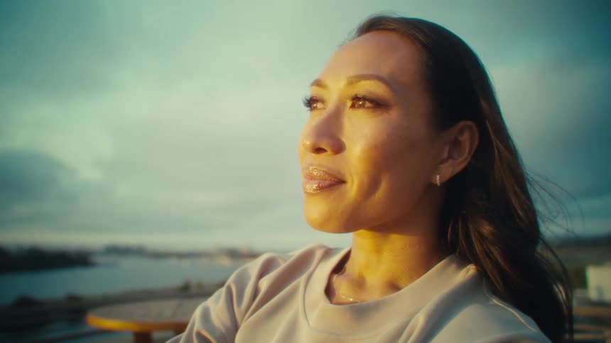 A smiling woman holds her phone out for a selfie in warm light