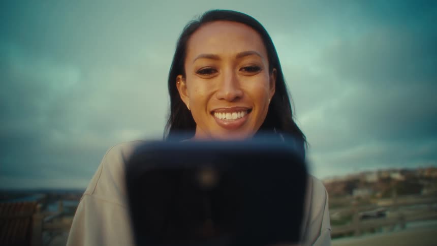 Close up of a young woman smiling while using her phone outdoors during daytime