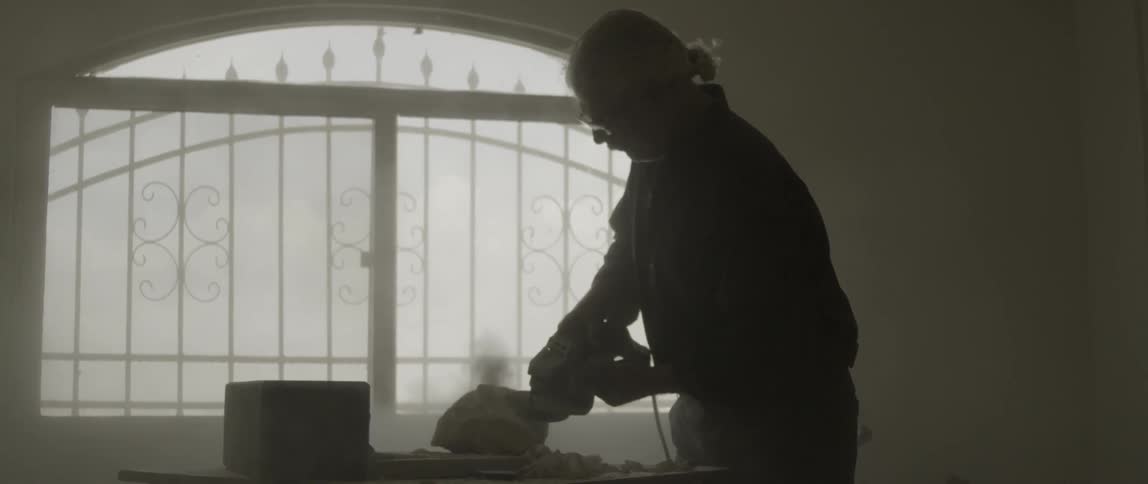 An elderly man uses a grinder on a sculpture