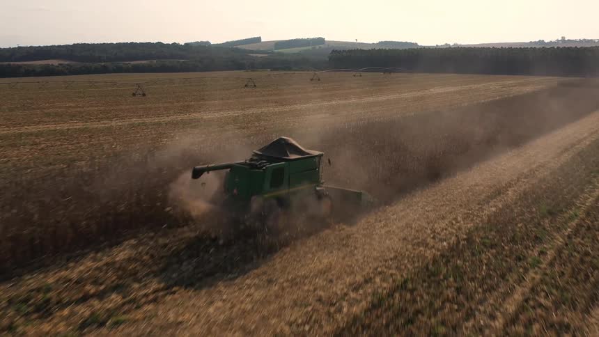 A combine harvester cuts through golden rows of crops leaving a trail of dust across the expansive field