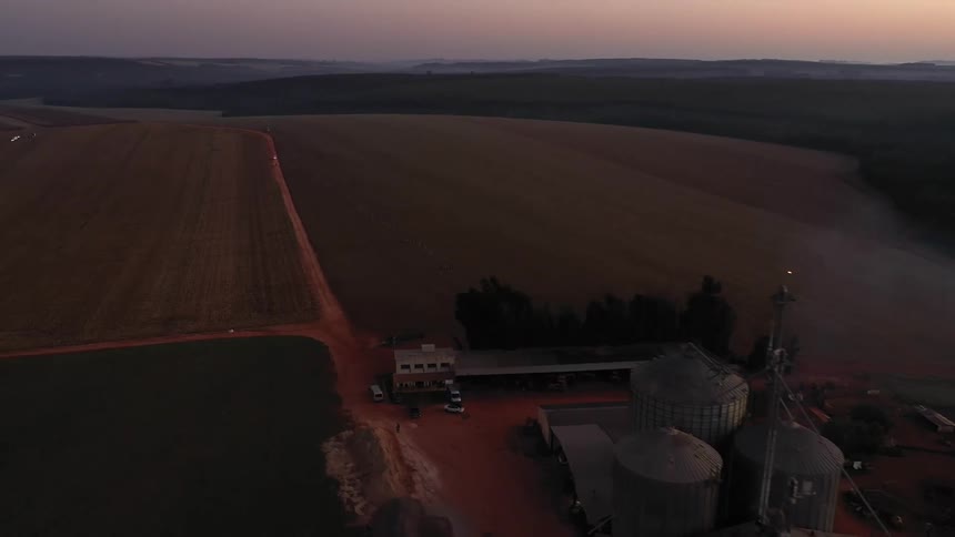 Aerial view of a rural grain processing facility beside vast farmland at dusk