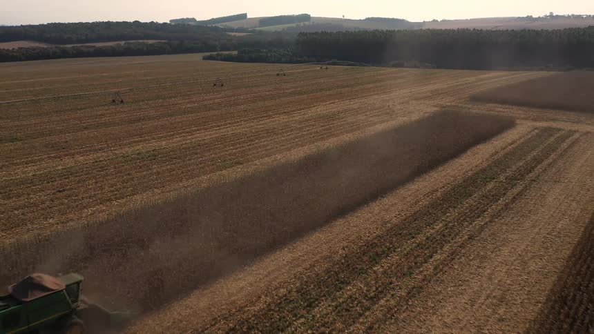 A dynamic aerial view captures a combine harvester diligently working through a vast agricultural field