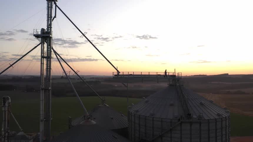 Grain silos and tall farming structures stand against a sunset sky