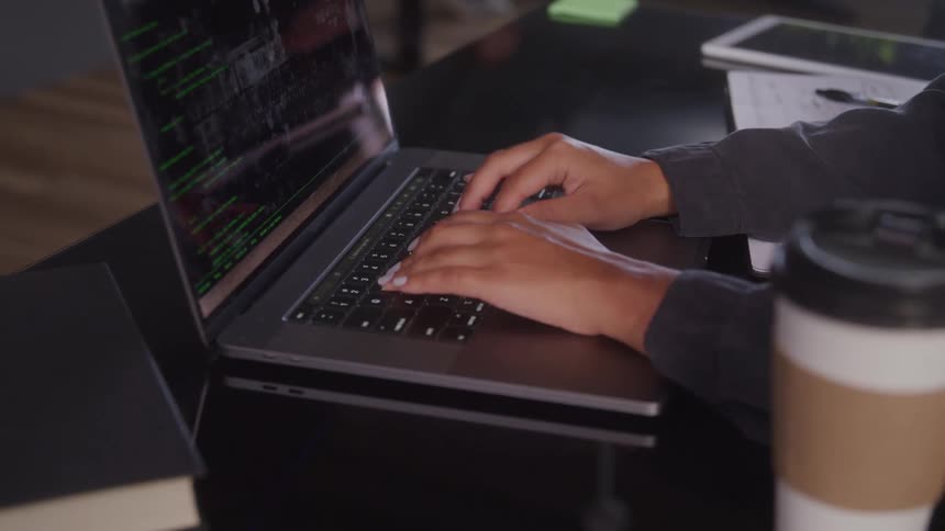 A person types on a laptop displaying code in a closeup indoor setting