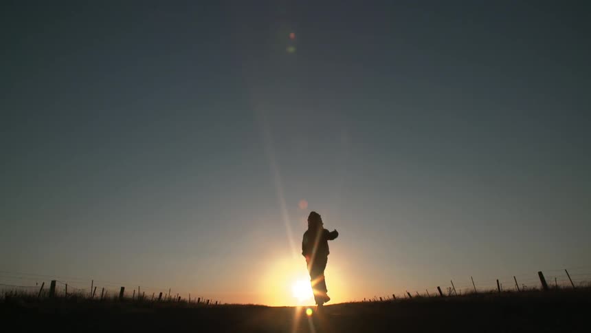A silhouetted boy runs towards the sunset