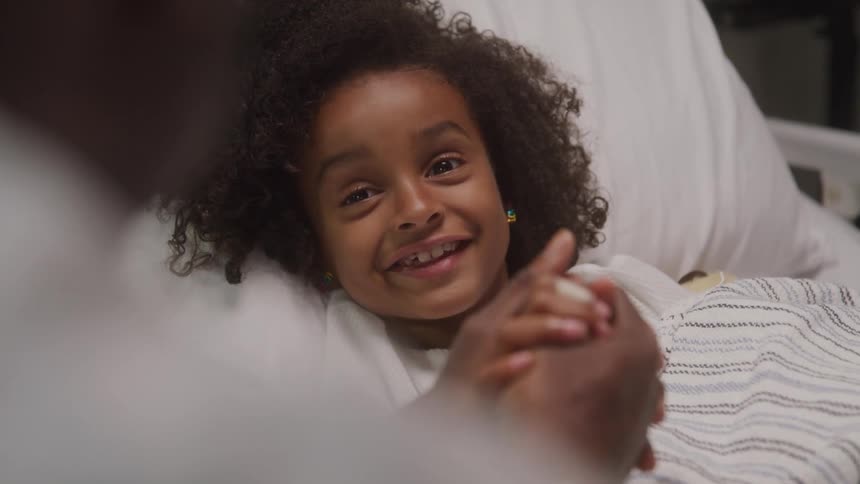 A nurse gently cares for a young girl resting in a hospital bed