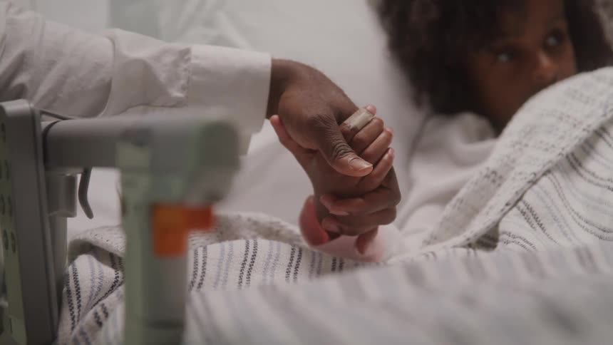 Adult staff holding hands with a curlyhaired child lying on a hospital gurney