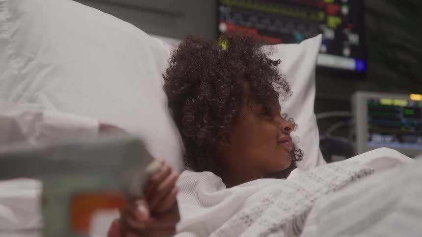 A child holds an adults hand while laying in a hospital bed