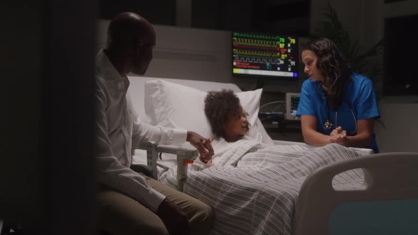 A child lies in a hospital bed as a parent and nurse offer comfort
