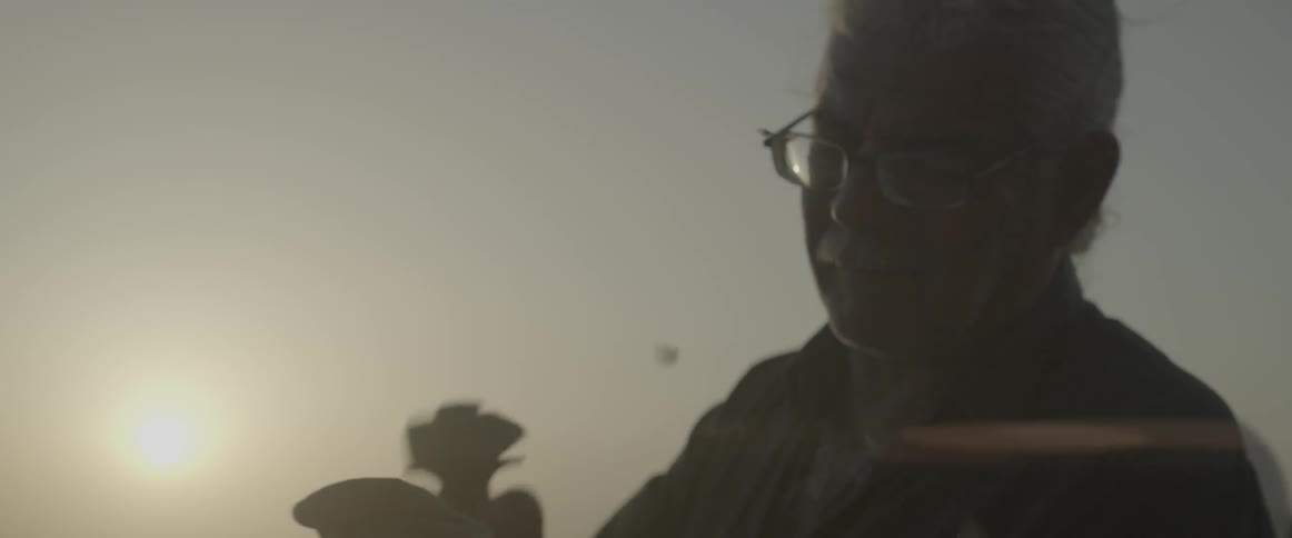 An elderly man works with a hammer and chisel outdoors