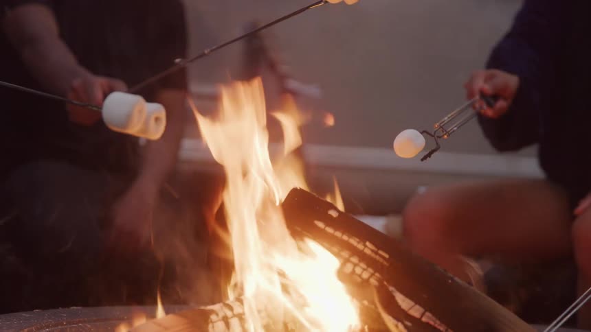 The video shows two individuals holding sticks with marshmallows over a campfire clearly enjoying the roasting process the flames of the fire are bright and central to the scene indicating a cozy outdoor gathering
