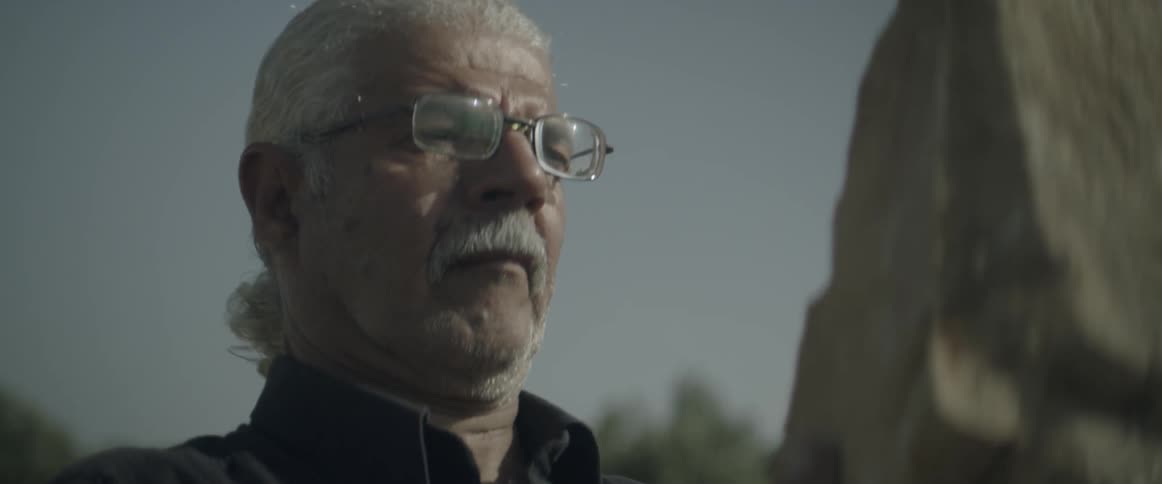 A man wearing glasses looks at a piece of wood
