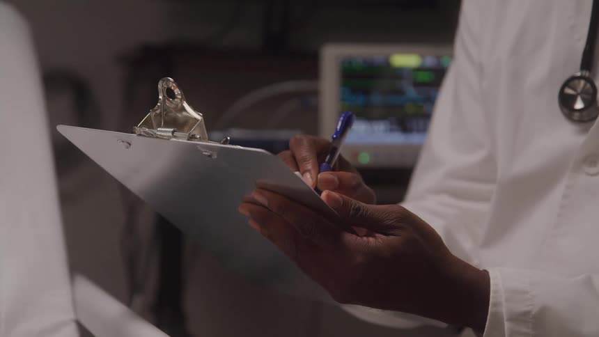 A doctor takes notes on a clipboard beside a hospital bed