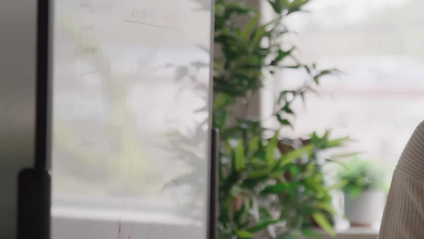 A person writes on a whiteboard with a marker in a modern indoor setting
