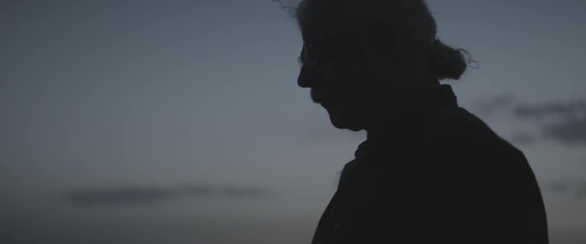 A man with curly white hair walks at dusk
