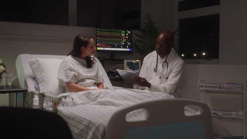 A doctor sits by a patients bedside reviewing medical documents with her