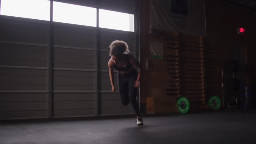 A woman is sprinting indoors during a workout in a gym