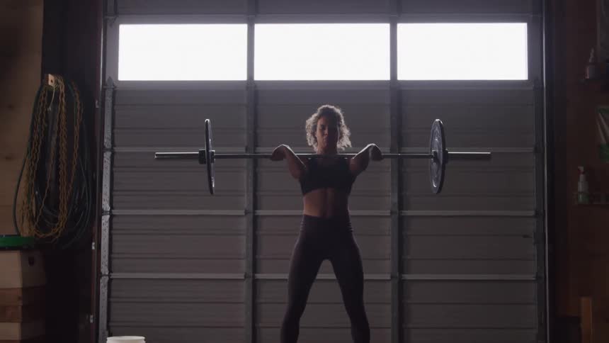 A woman lifts a barbell in a dimly lit gym