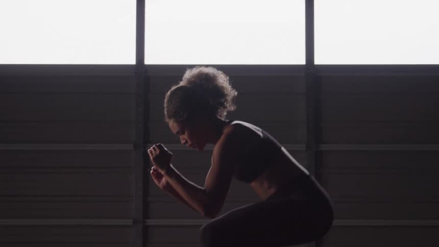 A woman does squats in a sunlit gym