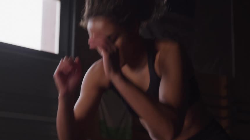 The video shows a woman with curly dark hair wearing a black tank top as she performs an intense exercise routine in a dimly lit gym the camera focuses on her focused expression as she pushes through the workout