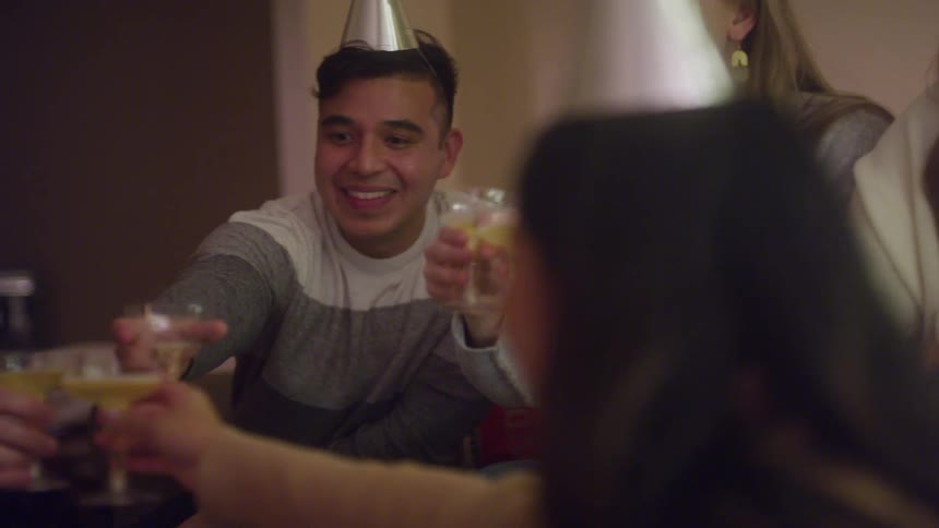 A group of friends wearing party hats toast with drinks and cheerful smiles
