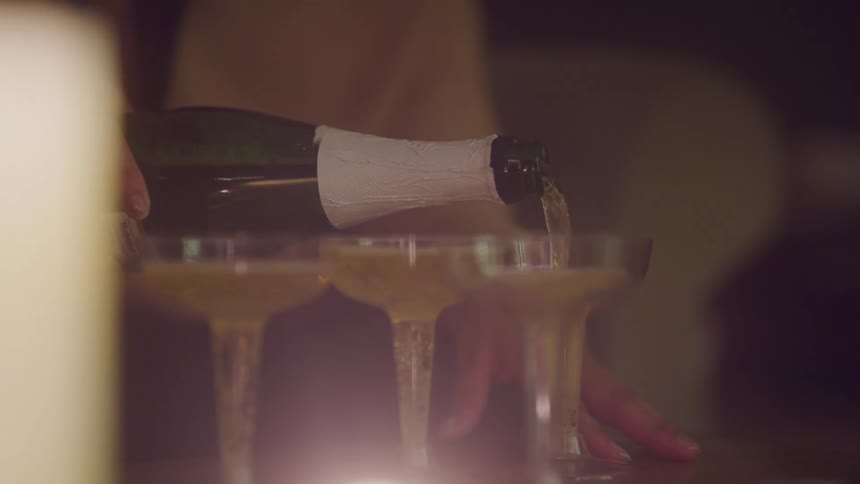 A person pours champagne into champagne glasses under warm ambient light