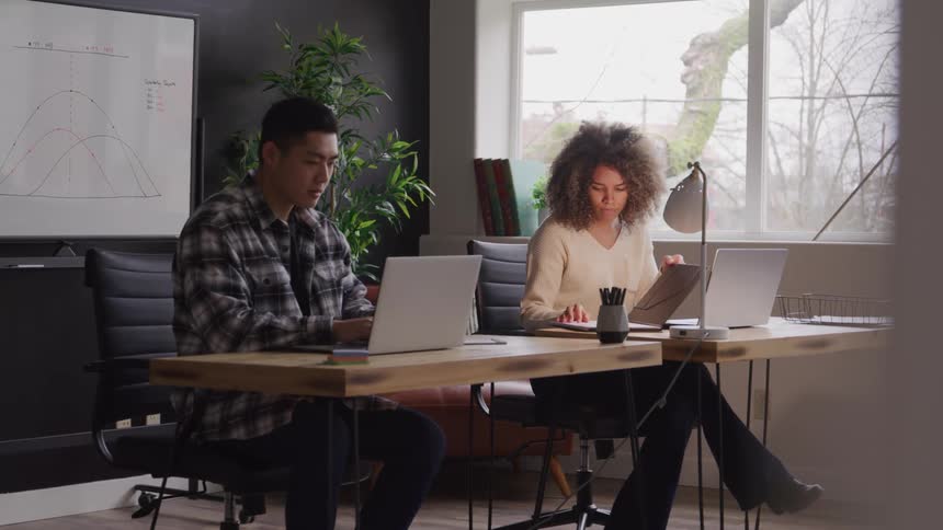 Man and a woman both in an office environment working on a laptop
