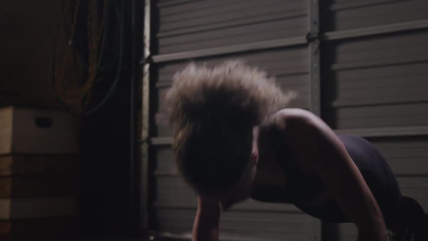 A woman performs pushups in a dimly lit garage gym