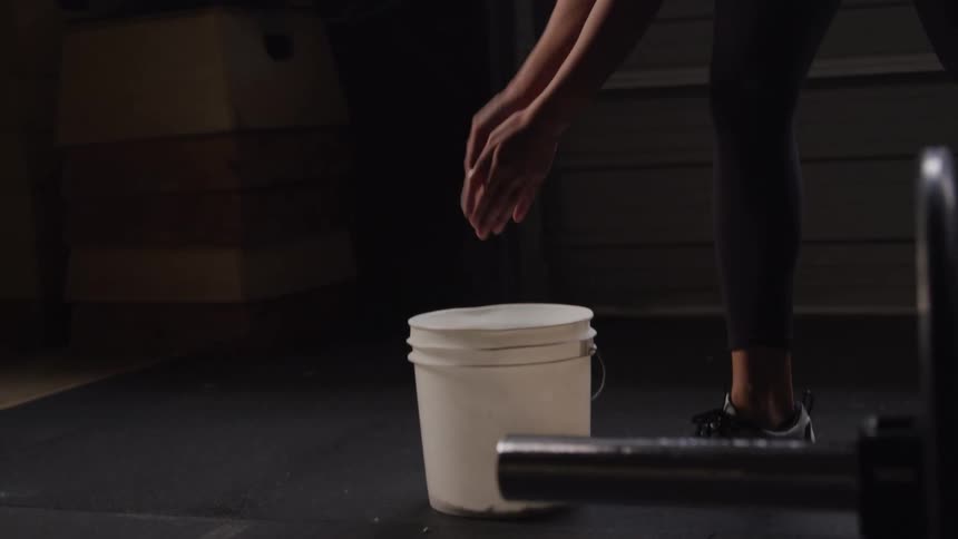 Woman putting her hands in a bucket of magnesium and clapping her hands together