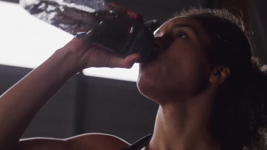 Woman in a gym environment drinking water from a bottle