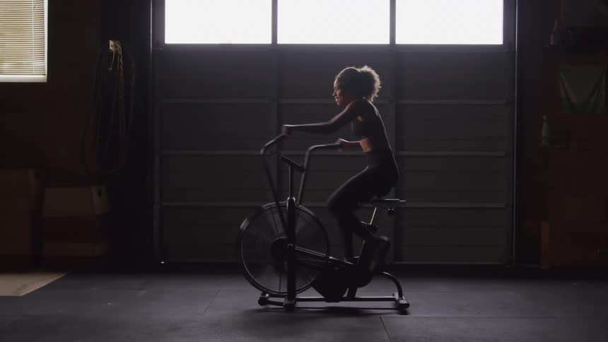 A young woman does cardio with a gym bike indoors during daytime