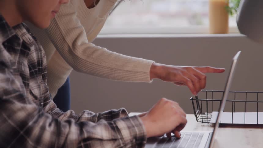 Woman in a work environment talking to a man who is sitting in front of a laptop