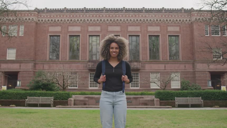 Happy female student standing on front lawn of campus university