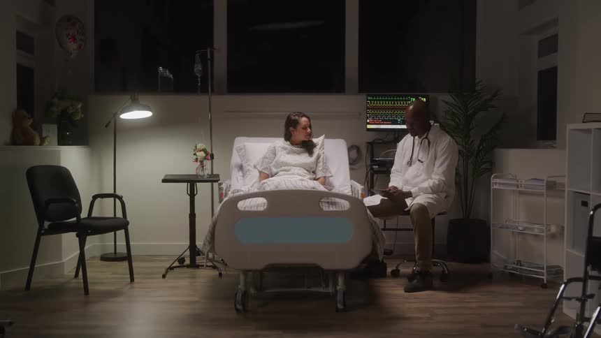Doctor sitting and talking with a patient who is in a hospital bed
