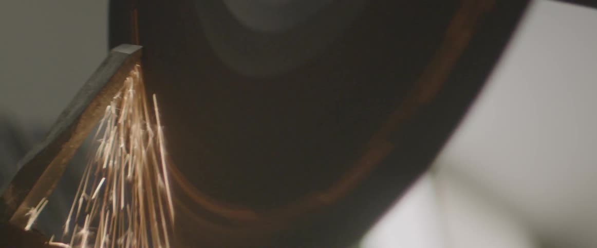 A rotating power tool is used to sharpen a chisel and gives off sparks