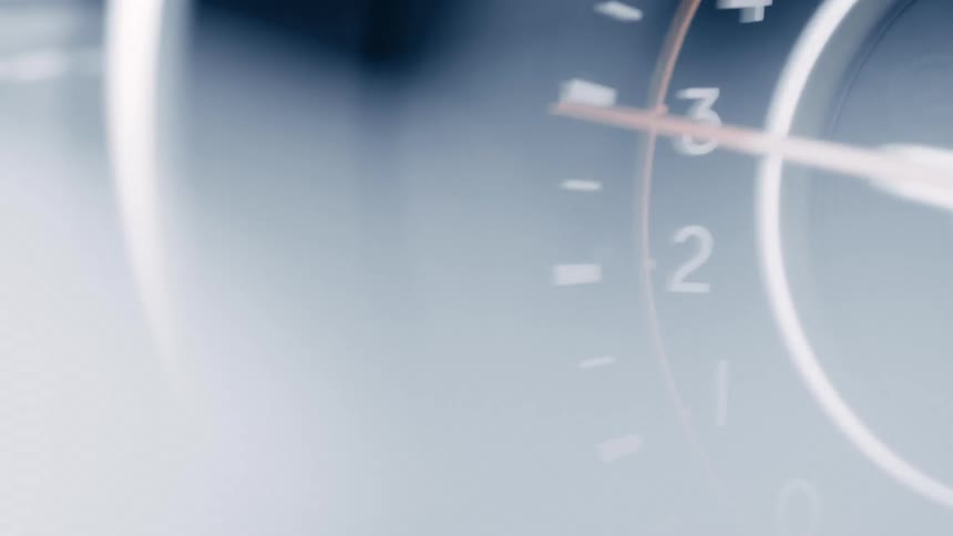 A blurry bluetinted closeup of a glossy clock shows faint numbers and a pointed hand