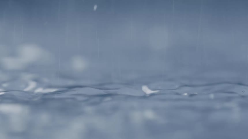 Multiple droplets fall from above and splash into the surface of clear water